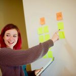 woman in gray sweater holding white and yellow sticky notes
